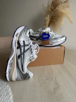 ASICS  silver och vita sneakers - Snygga ASICS GEL-1130 sneakers i silver, vitt och svart med mesh och syntetmaterial. Skorna har Ortholite-innersula och klassisk retrodesign med svarta detaljer längs sidorna. Perfekta för dig som gillar sportig och trendig stil.