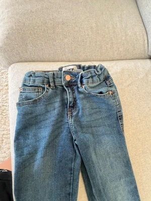 Blå raka jeans med hög midja/bootcut  - Säljer ett par klassiska blå jeans med rak passform och hög midja. Jeansen har fem fickor, kopparfärgade nitar och kontrastsömmar. Tillverkade i denim med en snygg tvätt. Perfekta för dig som gillar en tidlös look.byxorna är för barn 