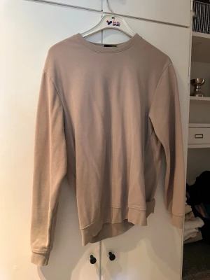 Beige oversized sweatshirt - En stilren beige sweatshirt med rund hals och långa ärmar. Oversized passform och ribbade muddar vid ärmslut och nederkant. Perfekt för en avslappnad look och enkel att matcha med jeans eller mjukisbyxor.