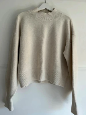Beige stickad tröja med låg polokrage & Other Stories - Beige stickad tröja med låg ribbad polokrage och ribbade muddar vid ärmslut och nederkant. Fint skick förutom att den är något nopprig. Djur och rökfritt hem.