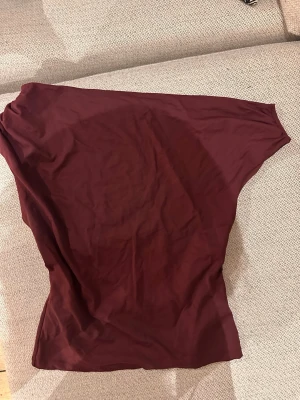 Vinröd topp från Gina Tricot - Vinröd topp från Gina Tricot i mjukt och stretchigt material. Modellen är ärmlös och är asymmetrisk. Endast använd en gång.