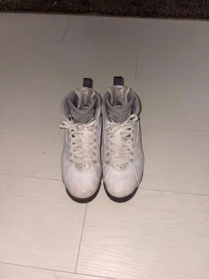 Vita höga sneakers från Jordan - Säljer ett par klassiska vita höga sneakers från Jordan med grå detaljer. Skorna har en ikonisk siluett, perforerade paneler och snörning framtill. Ovandelen är i läder och de har en robust sula som ger bra grepp. Perfekta för dig som gillar streetwear och sportig stil.