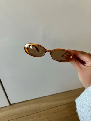 Le specs solglasögon caramel  - Snygga solglasögon från Fila med transparent orange båge och rundade glas. Perfekt accessoar för att lyfta din stil med en cool retrovibe. Märkeslogga på sidan av bågen ger en extra touch.