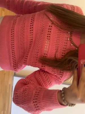 Rosa stickad tröja med hålmönster - Säljer en söt rosa stickad tröja med hålmönster och ribbade muddar. Tröjan har rund halsringning och långa ärmar. Perfekt för dig som gillar färg och vill ha något bekvämt och trendigt i garderoben.