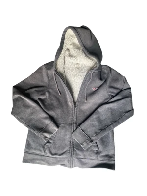 Hollister hoodie  - Mysig grå zip-hoodie från Hollister med vitt teddyfoder i huvan. Klassisk modell med dragsko, två fickor fram och broderad logga på bröstet. Perfekt för kalla dagar när du vill vara både bekväm och snygg.