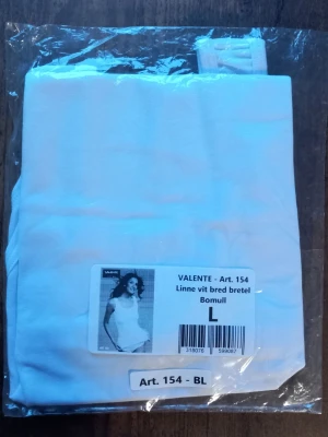 Vit linnetopp från Valente storlek L  - Säljer en klassisk vit linnetopp från Valente med breda axelband. Toppen är gjord i mjuk bomull och har en enkel, rak form som passar perfekt till jeans eller shorts. Perfekt för dig som gillar basic och stilrent. Storlek L