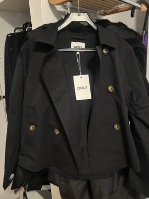 Svart trenchcoat  - Svart svart trenchcoat dubbelknäppning. Helt oanvänd med lappen kvar på, endast testad. Säljer då den är för stor för mig men för krångligt att skicka tillbaka. Storlek S. 