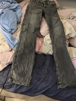 Grå låga utsvängda jeans med tvättad look - Säljer ett par grå jeans och snyggt tvättad effekt. Klassisk femficksmodell med vita kontrastsömmar. Perfekta för dig som gillar en avslappnad och stilren vibe. Materialet är denim.en knapp som saknas på bakfickan och dom har gått sönder en gång men de är lagat och syns inte 