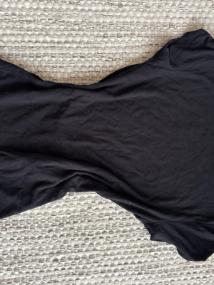 Svart t-shirt med utskuren rygg från Gina tricot  - En enkel svart t-shirt med en urringad rygg och korta ärmar. Perfekt att matcha med jeans eller kjol för en clean look. Materialet känns mjukt och lätt, troligen bomull. Passformen är normal och modellen är klassisk.