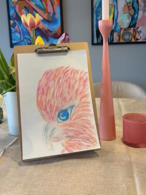 Färgglad teckning av fågel - Unik handritad teckning av en fågel i profil med intensivt blått öga och fjädrar i rosa, orange och gula toner. Gjord på vitt papper med färgpennor, perfekt som dekoration till rummet eller som personlig present.