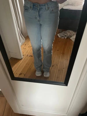 Ljusblå raka jeans med mid midja - Säljer ett par ljusblå jeans med raka ben och mid midja. Jeansen har klassiska fem fickor och stängs med knappar. Perfekta för en avslappnad och trendig look.
