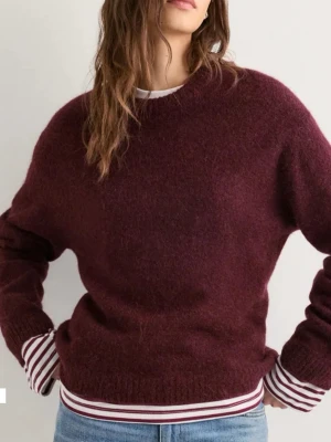 Vinröd stickad tröja från Gina Tricot - Mysig vinröd stickad tröja från Gina Tricot med rund halsringning och långa ärmar. Tröjan har en fluffig struktur och ribbstickade muddar vid ärmslut och nederkant. Perfekt för lager-på-lager och passar till jeans eller kjol. Sällan använd!