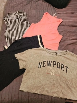 Toppar H&M Divided XS/S - 4-pack toppar från H&M Divided XS/S  Säljer fyra snygga toppar: en grå croppad t-shirt med Newport 1981-tryck (XS), en svart croppad t-shirt med vita ränder på ärmarna (S), en rosa ärmlös croppad topp och en svartvit randig polotopp utan ärmar. Perfekt för dig som gillar att mixa stilar och färger.  Kan även hämtas I Partille  E1