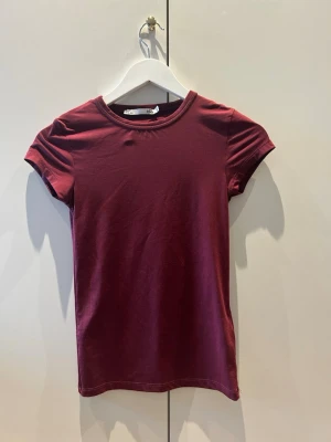 Vinröd t-shirt - Enkel och stilren vinröd t-shirt från lager 157 med rund halsringning och korta ärmar. Perfekt basplagg i garderoben och lätt att matcha med andra kläder. Tillverkad i ett mjukt och stretchigt material. Materialet är lite som en tränings T-shirt.