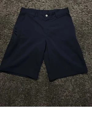 Mörkblå shorts från Puma - Snygga mörkblå shorts från Puma med klassisk passform och diskret logga på baksidan. Shortsen har knapp och dragkedja framtill samt två bakfickor. Perfekta för en stilren och sportig look.