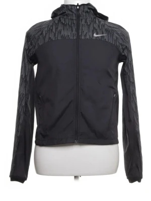 Svart Nike vindjacka med mönster - Svart vindjacka från Nike med grått mönster på axlar, ärmar och huva. Jackan har hel dragkedja, två sidofickor med dragkedja och en sportig look. Perfekt för blåsiga dagar och träning utomhus. Materialet är lätt och vattenavvisande. Pris kan diskuteras vid snabb affär.