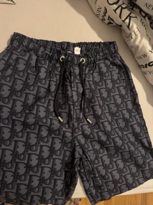 Mönstrade blå shorts med snörning - Snygga blå shorts med ett grafiskt mönster och elastisk midja med snörning. Perfekta för sommaren och har en avslappnad passform. Materialet känns lätt och bekvämt, och shortsen har en modern vibe som passar till många olika stilar.