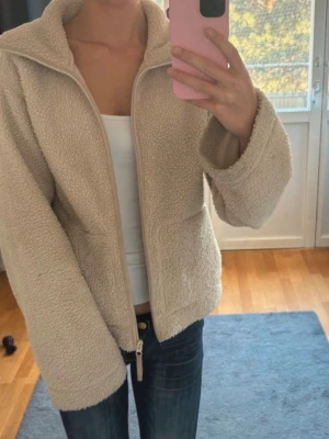 Beige teddyjacka - Mysig och söt beige teddyjacka med dragkedja framtill och två stora fickor. Jackan har en avslappnad passform och är tillverkad i mjukt, fluffigt teddy-material som håller dig varm. Perfekt för kyliga dagar och enkel att matcha med jeans eller leggings.🤍🧸