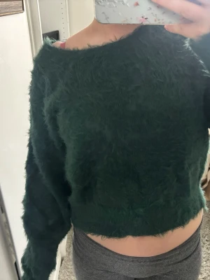 Grön fluffig stickad tröja BikBok - Mysig grön stickad tröja från BikBok med fluffig textur och croppad passform. Tröjan har långa ärmar och rund halsringning, perfekt för dig som gillar en trendig och bekväm stil. Materialet är mjukt och ger en cool look. Säljer då den inte kommit till användning