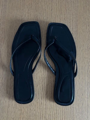 Svarta fyrkantiga sandaler - Svarta flipflops i någon skinimmitation från Zara i storlek 39. Litet skav på ena skon vilken syns på bilden, men inget som syns då man har de på sig.