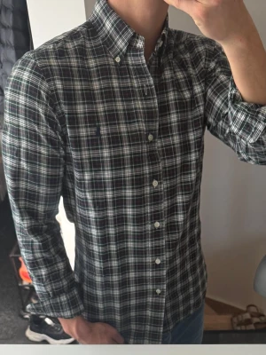 Rutig långärmad skjorta från Polo Ralph Lauren - Snygg rutig skjorta från Polo Ralph Lauren i mörkblått, grönt och vitt. Skjortan har klassisk krage, knappar hela vägen och lång ärm. Perfekt för dig som gillar en tidlös och stilren look.