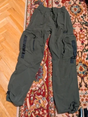 Olivgröna cargobyxor från H&M - Olivgröna cargobyxor från H&M i 100% bomull. Byxorna har flera stora fickor på sidorna, svarta detaljer och dragsko vid benslut och midja. Perfekta för en avslappnad och trendig streetstil.
