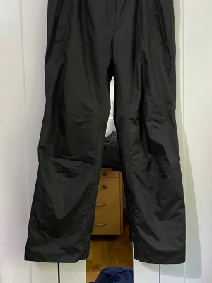 Svarta täckbyxor med raka ben - Svarta täckbyxor med raka ben och resår i midjan. Byxorna har en enkel design med sidfickor och är tillverkade i ett vattenavvisande material som passar perfekt för kalla dagar utomhus.