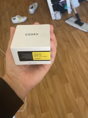 COSRX Advanced Snail 92 Cream - COSRX Advanced Snail 92 All in one Cream i vit fyrkantig förpackning. Krämen är känd för sin återfuktande och lugnande effekt, perfekt för dig som vill boosta din hudvårdsrutin. Innehåller snigelsekretfiltrat och passar de flesta hudtyper.