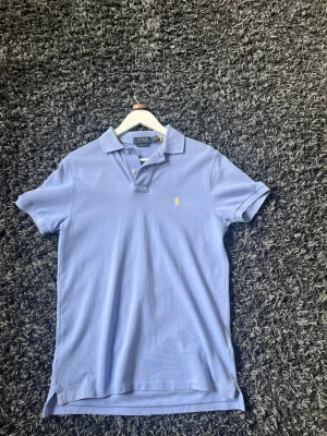 Ljusblå pikétröja från Polo Ralph Lauren - Klassisk ljusblå pikétröja från Polo Ralph Lauren. Perfekt för en stilren och avslappnad look. Så gott som nyskick, använd ett par gånger. Hör av er vid frågor!