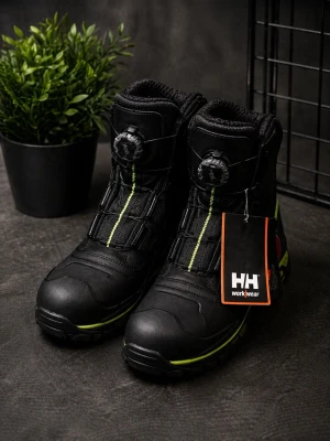 Svarta kängor från Helly Hansen - Svarta kängor från Helly Hansen Workwear med gröna detaljer och BOA-snörning. Grov Vibram-sula för extra grepp och slitstyrka. Hög modell med vadderad insida och robust design, perfekt för tuffare miljöer. Märkeslogga på sidan och etikett framtill.