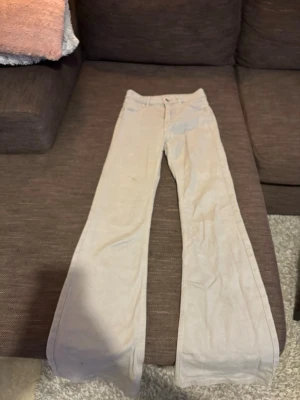 Beige utsvängda jeans - Säljer ett par beige jeans med utsvängda ben och klassisk femficksdesign. Jeansen har normal midja och stängs med knapp och dragkedja. Perfekta för dig som gillar en retroinspirerad look och vill ha ett par neutrala byxor i garderoben.