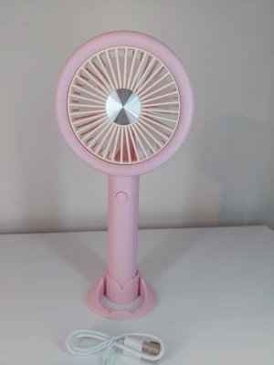 Rosa portabel USB-fläkt - Denna bärbara USB-fläkt är designad för att ge svalka. Den har en lätt konstruktion och kan användas både handhållen och placeras i det medföljande stativet. Fläkten laddas via USB och har en enkel knapp för användning.