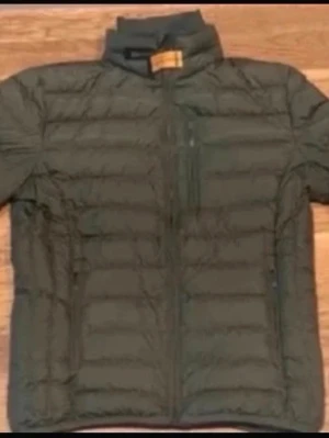 Grön quiltad dunjacka - Snygg mörkgrön dunjacka med quiltad design och dragkedja framtill. Jackan har hög krage och två sidofickor med dragkedja. Perfekt för kyliga dagar och enkel att matcha med olika outfits. Har inte använt den många gånger, man kan säga att jackan är ny.