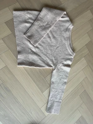 Beige stickad tröja med ribbade detaljer - Mysig beige stickad tröja med båtringning och ribbade muddar vid ärmslut och nederkant. Perfekt för lager-på-lager och enkel att matcha med jeans eller kjol. Klassisk och stilren design som passar till många tillfällen.