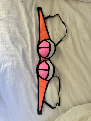 2016 Triangl bikini topp  - Cool bikiniöverdel i orange, rosa och vit med svarta kontrastkanter. Sportig design med vadderade kupor och justerbara axelband. Perfekt för stranden eller poolen och ger en riktigt poppig look. Köpt på Sellpy men aldrig använd 