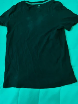  basic t-shirt från H&M - En enkel mörkblå t-shirt från H&M Basic, tillverkad i mjuk bomull. T-shirten har rund halsringning och korta ärmar, perfekt för en clean och avslappnad stil.