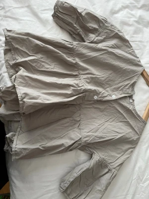 Beige volangblus med knappar - Luftig beige blus med volangdetaljer och trekvartsärm. Blusen har knappar framtill och en avslappnad, loose passform. Perfekt för en chill och stilren look.