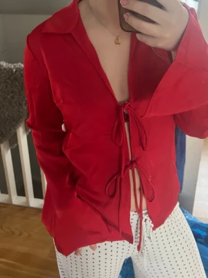 Röd satinblus från NA-KD - Snygg röd blus i satin från NA-KD med knytning framtill. Perfekt för att ge en färgklick till din outfit. Blusen har långa ärmar och en elegant design som passar till många tillfällen.