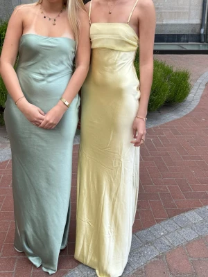 Peppermayo Ljusgul långklänning i satin - Elegant ljusgul långklänning i satin från peppermayo perfekt till bal eller annan festlig tillställning. Klänningen har en slät, figurnära passform och en mjuk glansig yta som ger en lyxig känsla.                                                                             Använd en gång och ingen syn på användning!