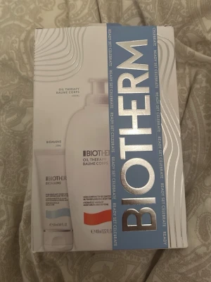 Biotherm Oil Therapy presentkit - Säljer ett Biotherm presentkit med Oil Therapy Baume Corps kroppslotion (400 ml) och Biomains handkräm (50 ml). Förpackningen är vit med silverdetaljer och blått band. Perfekt för dig som vill ha återfuktande hudvård med lyxig känsla.