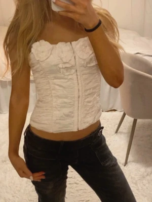 Vit korsett-topp från Zara - Superfin vit korsett-topp med stora tygblommor upptill och lätt rynkad effekt. Litet märke inuti men inget som syns🤍