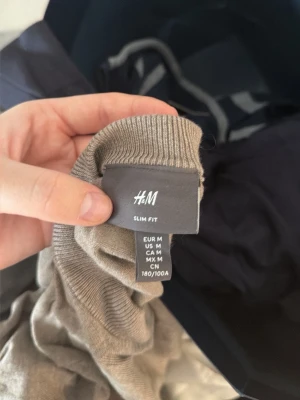 Beige slim fit stickad tröja H&M - Säljer en beige stickad tröja från H&M i slim fit-modell. Tröjan har rund halsringning, långa ärmar och ribbade muddar vid ärmslut och nederkant. Perfekt för dig som gillar en enkel och stilren look.