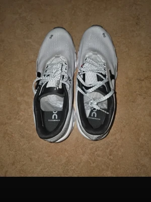 On Cloudmonster vita sneakers - Säljer ett par On Cloudmonster sneakers i vitt med svarta detaljer och cool sula. Skorna har mesh-överdel, vita och svarta snören samt logga på sidan och plösen. Riktigt snygg och sportig design som sticker ut.