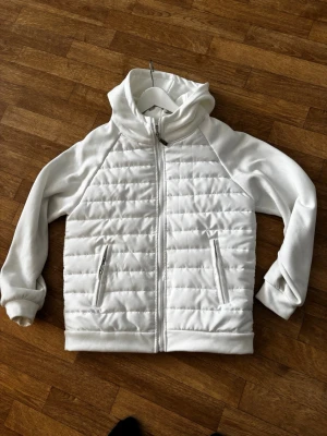 Vit quiltad jacka  - Snygg vit jacka med quiltad framsida och dragkedja. Jackan har två fickor med dragkedja och en hög krage. 