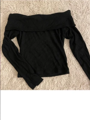 Svart offshoulder ribbad topp - Svart ribbad topp med offshoulder-modell och långa ärmar. Snygg och enkel att styla till olika outfits, perfekt för dig som gillar trendiga och stilrena plagg. Storlek S. Från Gina tricot.
