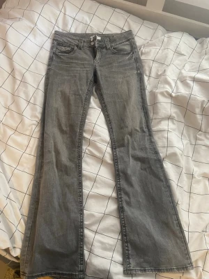 Grå bootcut jeans med låg midja - Säljer ett par grå bootcut jeans med låg midja och klassiska fem fickor. Jeansen har en lätt tvättad look och vida ben från knät och ner. Perfekta för dig som gillar retrostil och vill ha ett par bekväma jeans med snygg passform.