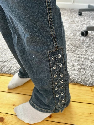 Bootcut jeans med snörning i sidan - Säljer ett par mörkblå jeans med snygg snörningsdetalj längs nedre delen av benen. Är inte så bra på att ta bilder men dom ör bootcut assnygga!! Säljer då dom inte kommer till använding (passar till folk som ör mellan 160-170 