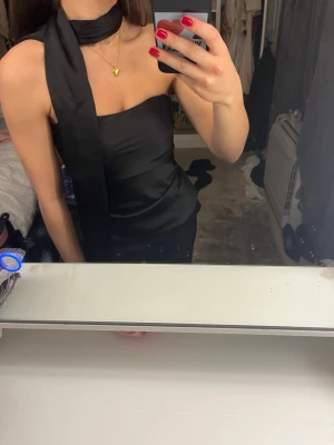 Svart axelbandslös satin topp Zara - Snygg svart axelbandslös topp i satin med en scarfdetalj runt halsen. Toppen har en croppad passform och glansigt material som ger en lyxig känsla. Perfekt för att skapa en trendig och elegant look.