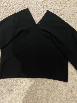 Svart v-ringad topp med lång ärm - Snygg svart topp med v-ringning och långa ärmar. Modellen är croppad och har en enkel, stilren design som passar till det mesta. Tillverkad i ett mjukt och stretchigt material för skön passform. Från Arket