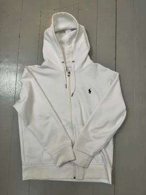 Ralph lauren zip hoodie - Hallå! Säljer en vit Ralph lauren zip hoodie. Köpte den för ca 2 år sedan: Då den var för stor, så tänkte jag att jag skulle växa i den. Dock har jag i princip aldrig använt den, så skicket är så gott som nytt! Skriv bara för fler bilder eller om du har några funderingar 